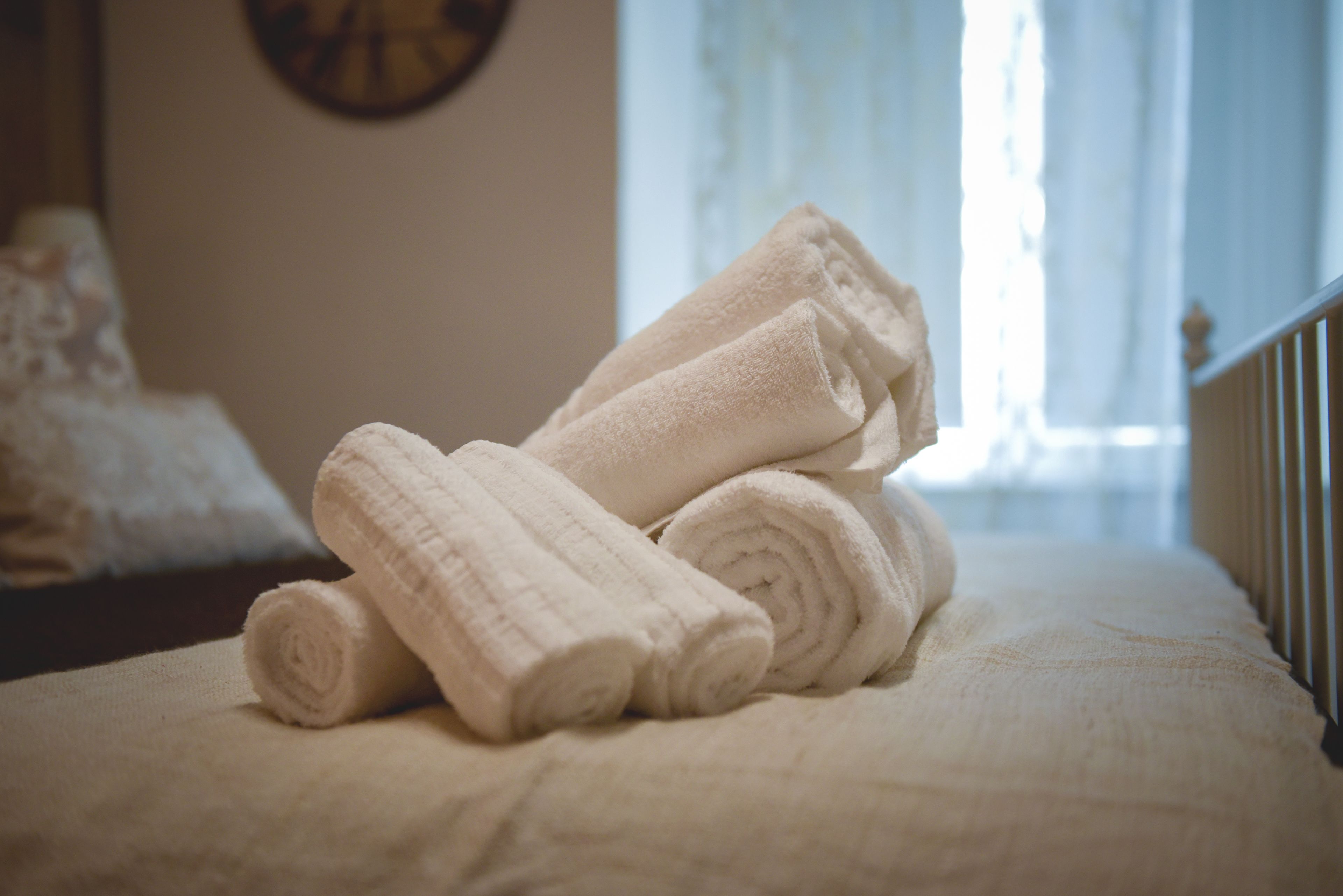 A bed with rolled white towels and a clock on the wall.