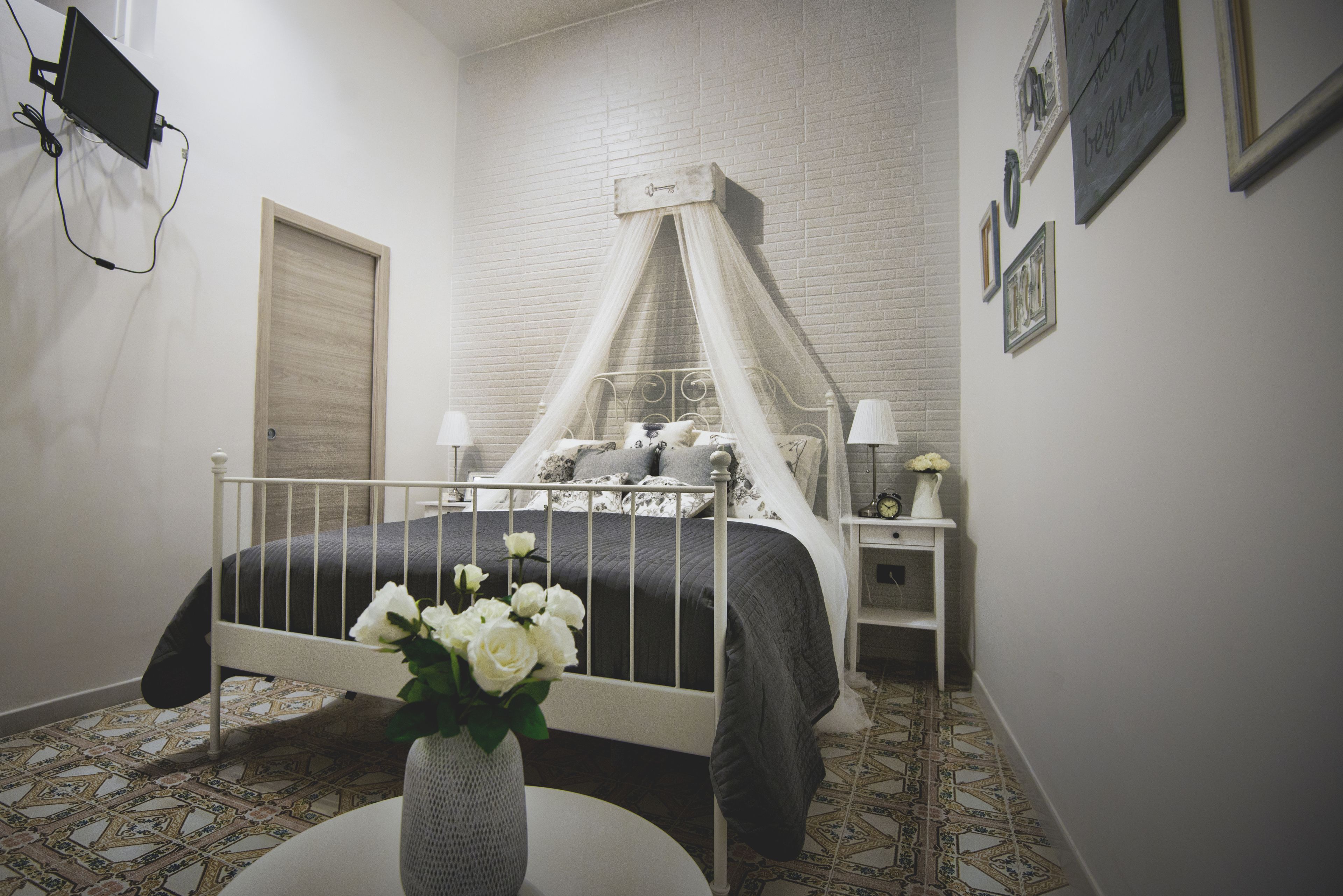 Un dormitorio con cama con dosel, una mesita de noche con lámpara y televisor montado en la pared.