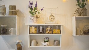 A kitchen with white shelves holding jars, a clock, and various kitchenware. - Elegant B&B Il Vicolo storico (Salerno)