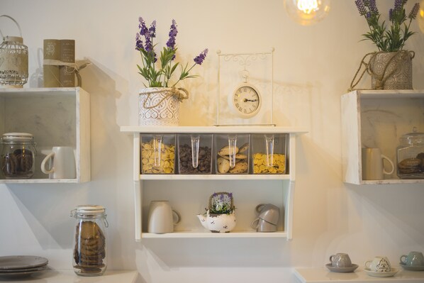 A kitchen with white shelves holding jars, a clock, and various kitchenware.