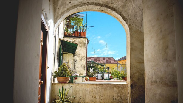 An arched doorway leading to a courtyard with potted plants and a view of buildings. - Elegant B&B Il Vicolo storico (Salerno)
