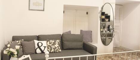 A modern living room with a grey sofa, decorative pillows, a small table with a vase of flowers, and a framed picture on the wall.