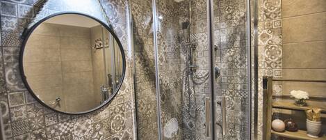 A bathroom with a glass-enclosed shower, a round mirror, and patterned tiles.
