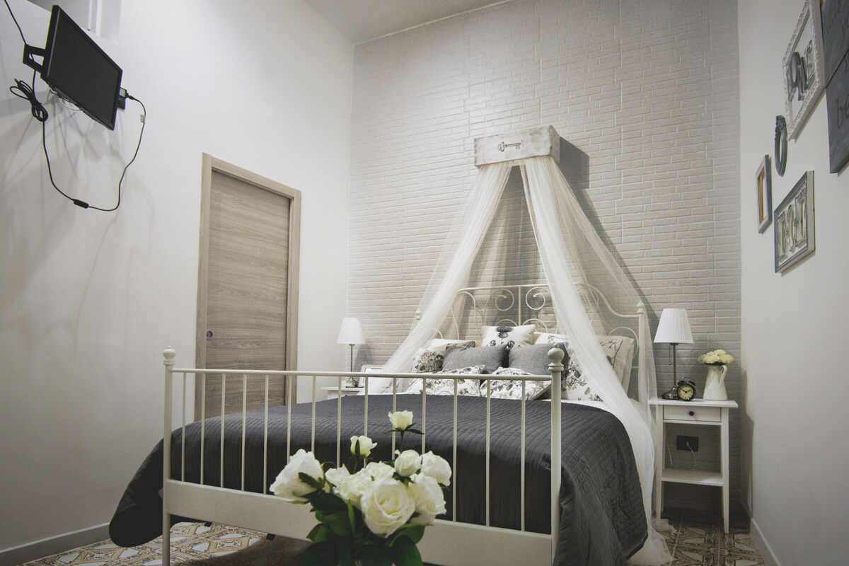 A bedroom with a four-poster bed, a bedside table with a lamp, and a wall-mounted TV.