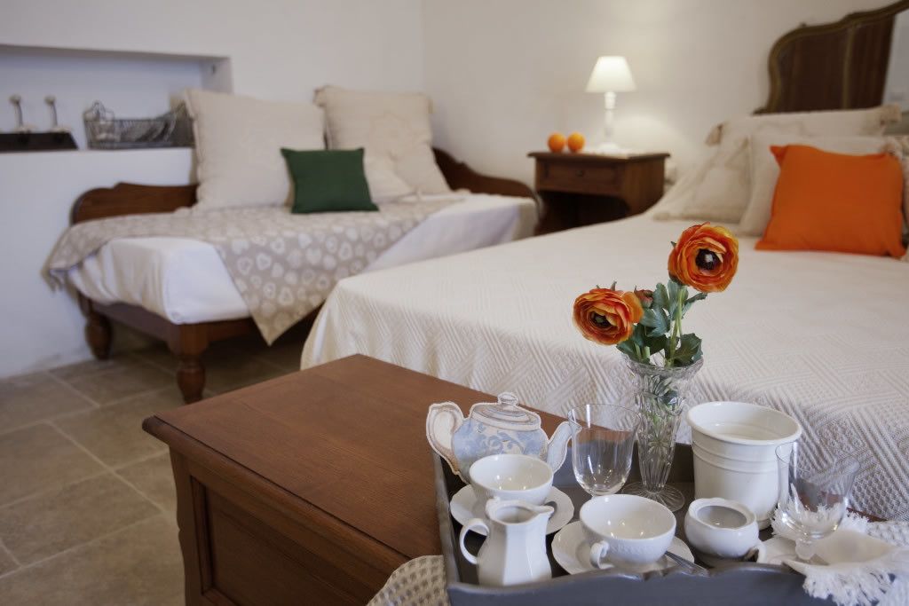 Une chambre d’hôtel avec deux lits, une table de chevet en bois, une table avec un service à thé et un vase rempli de fleurs.