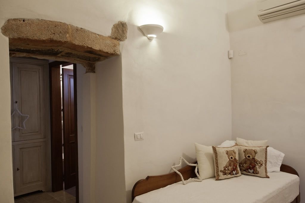 A bedroom with a bed, two pillows with teddy bear designs, a wall-mounted light, and a door leading to another room.