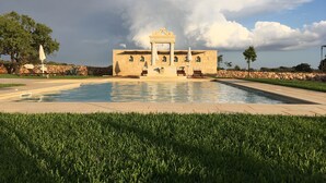A pool with a stone building in the background, surrounded by greenery. - Masseria Cisternella (Alliste)