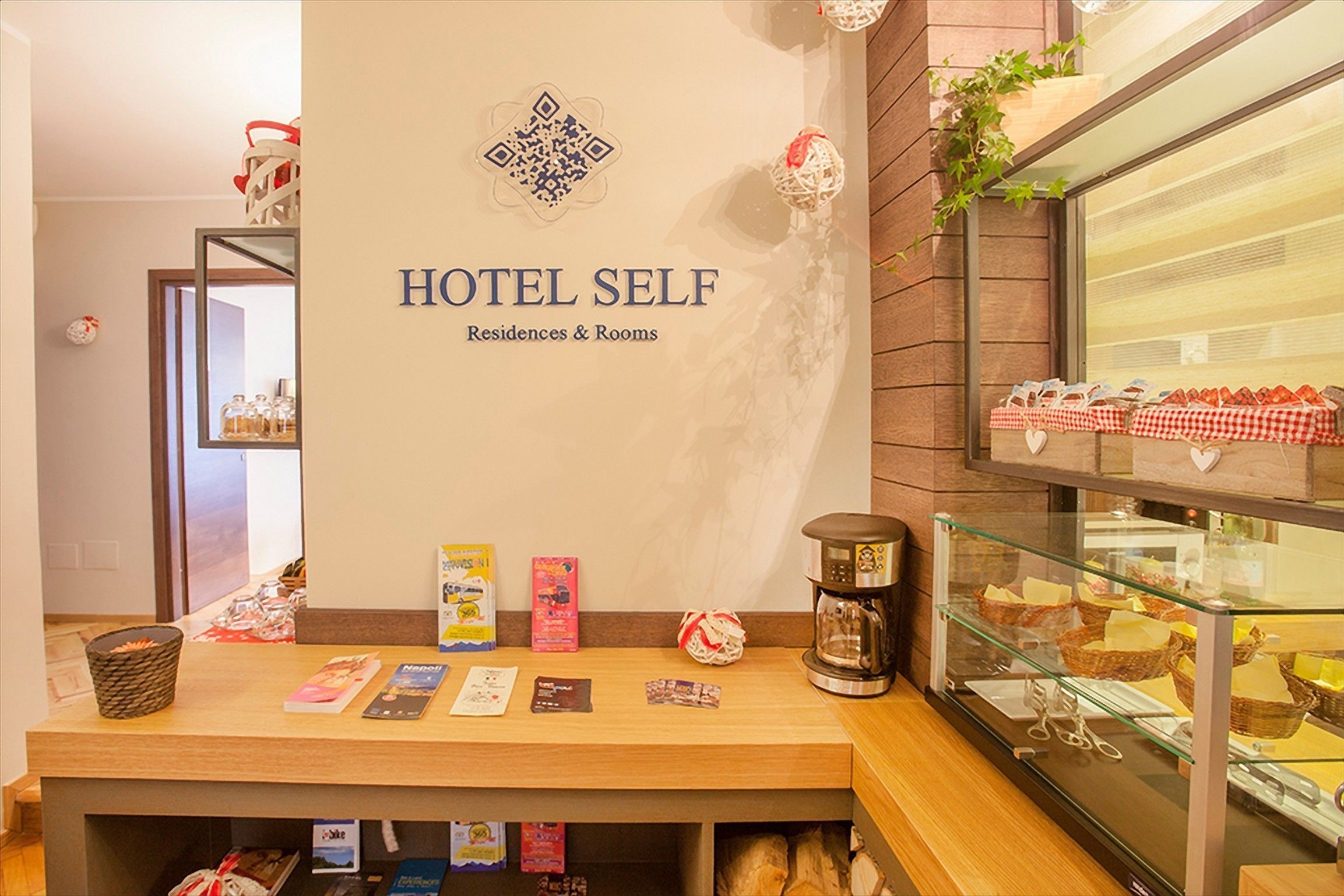 A hotel self-service area with a reception desk, a coffee machine, and a display case with food items.
