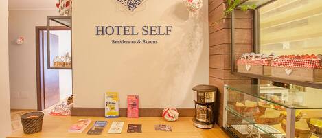 A hotel self-service area with a reception desk, a coffee machine, and a display case with food items.
