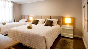 A hotel room with two beds, a wooden nightstand, a lamp, and a rug. - Apartamentos Charm Centro Gramado (Gramado)