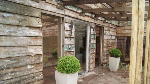 A rustic wooden building with large glass doors and a tiled patio area. - Apartamentos Charm Centro Gramado (Gramado)
