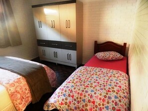 A bedroom with two single beds, a wardrobe, and a brick wall.