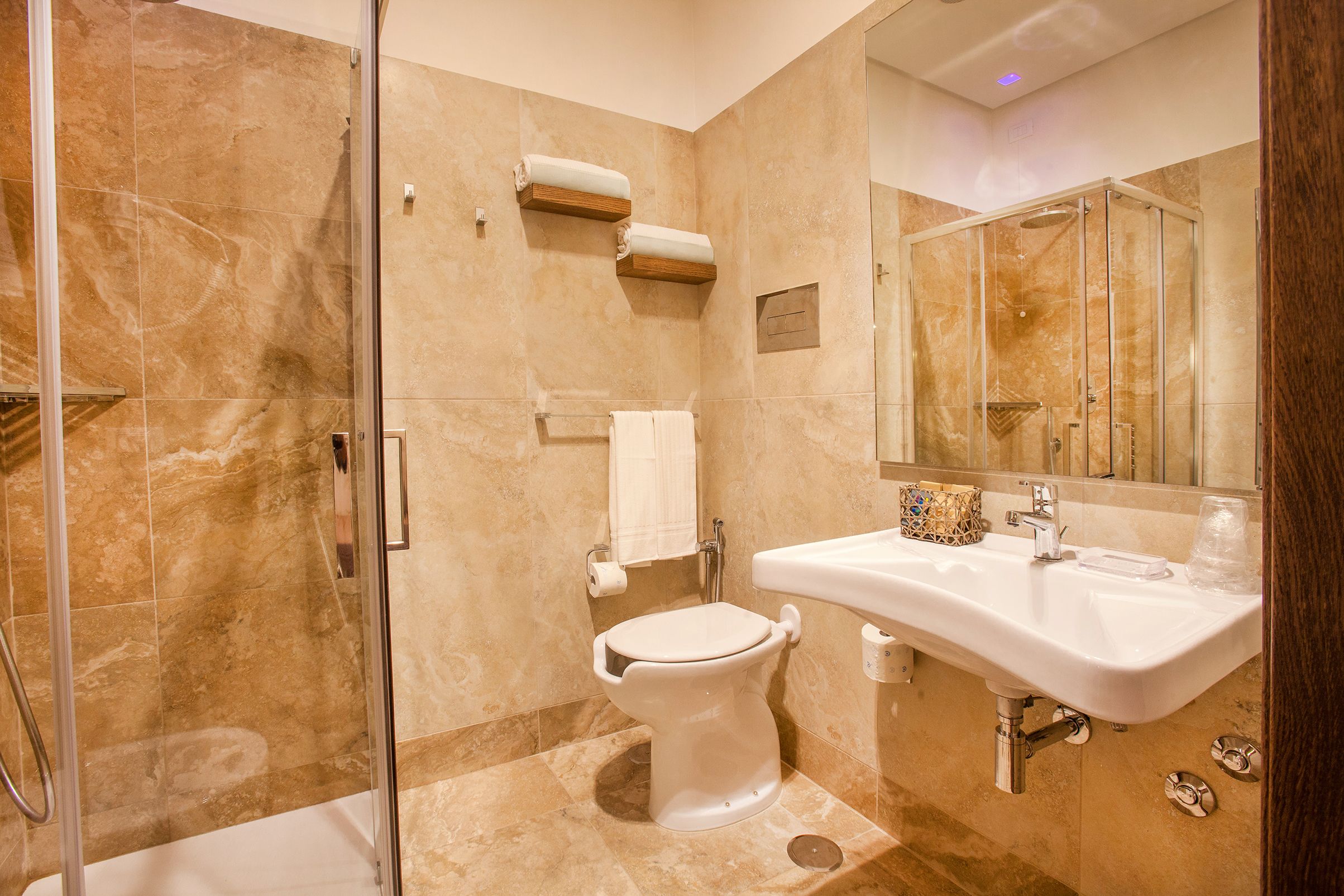 Un baño moderno con ducha de mampara de vidrio, lavamanos blanco y suelo de mármol.