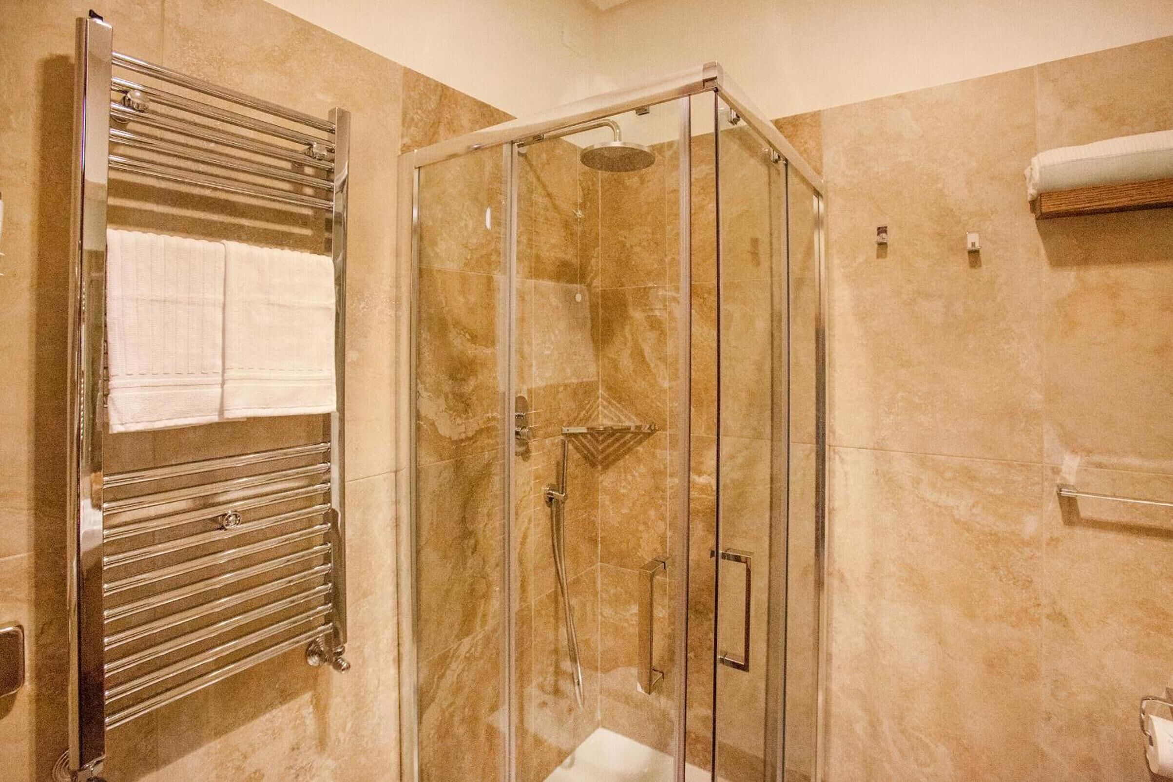 A bathroom with a glass-enclosed shower, a towel rack, and a marble-tiled wall.