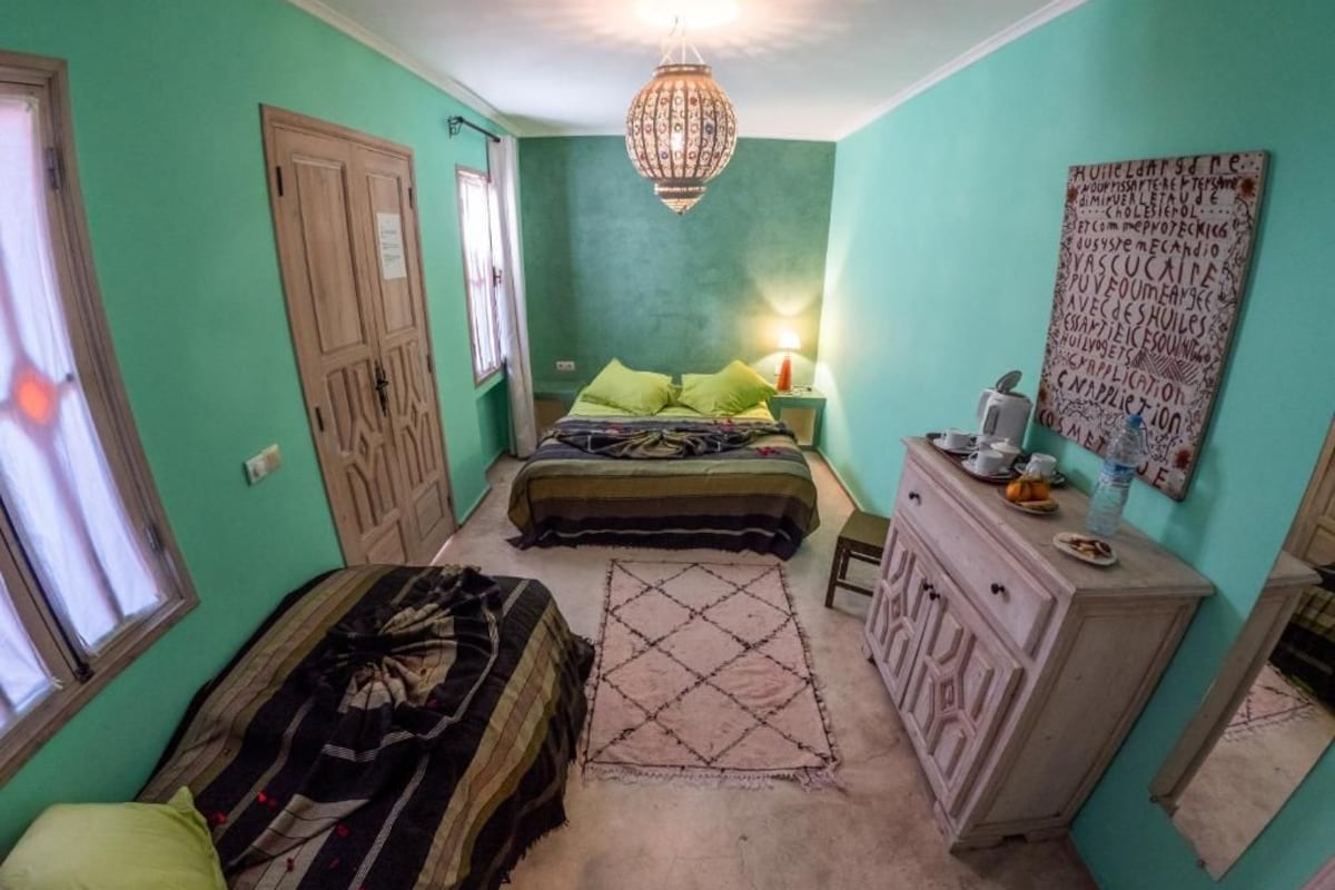 Quarto com cama, penteadeira, luminária suspensa e parede com texto.