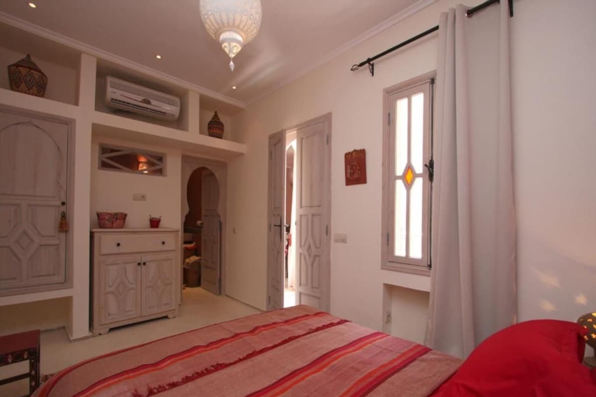 Quarto com cama, guarda-roupa, espelho e janela com cortinas.