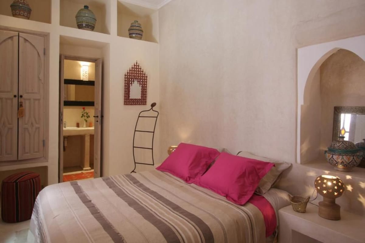 Quarto com cama, guarda-roupa, espelho e objetos decorativos.