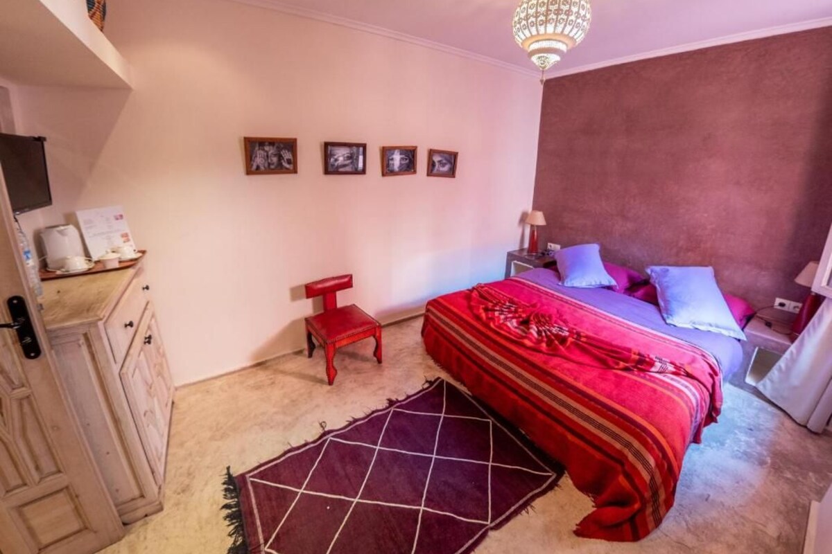 Quarto com cama, mesa de cabeceira, abajur e lustre.