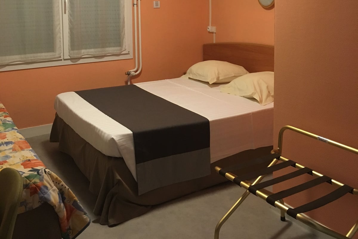 Une chambre avec un lit, une fenêtre avec des rideaux, une table de chevet et une chaise.