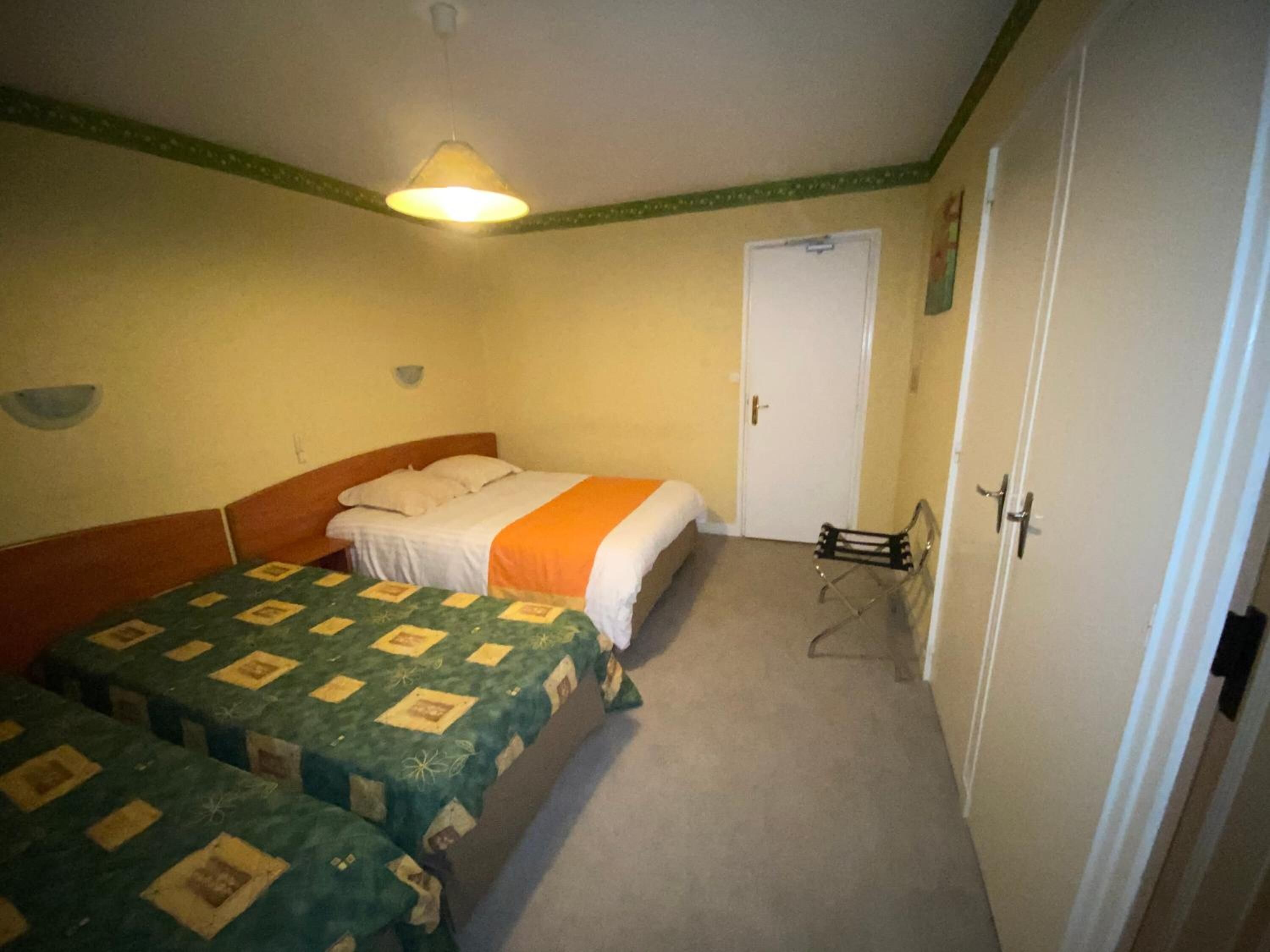 Una habitación con dos camas individuales, una mesita pequeña, una silla, una puerta y una lámpara colgante.