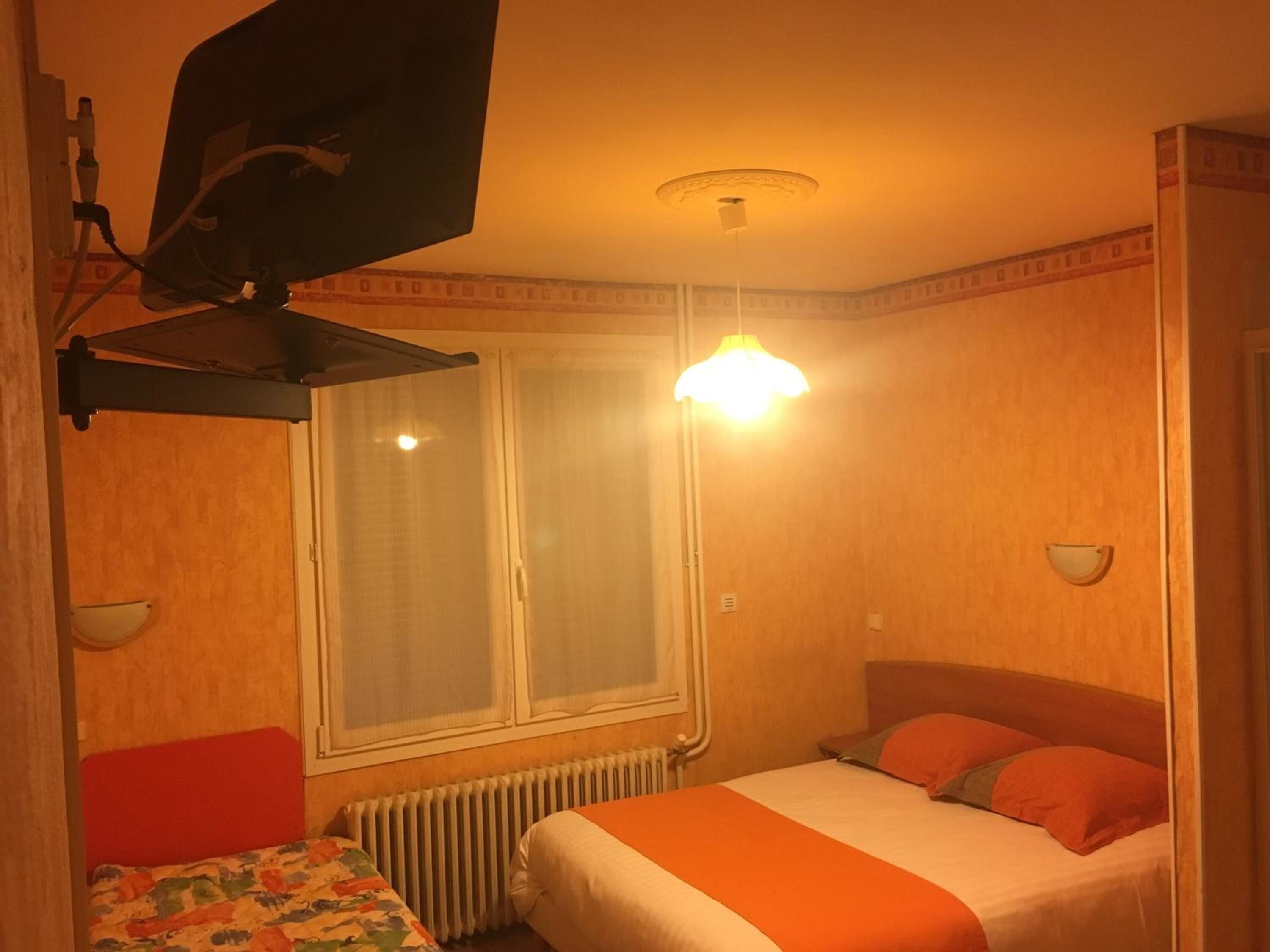 A small, cozy hotel room with a single bed, a small table, a radiator, and a window with curtains.