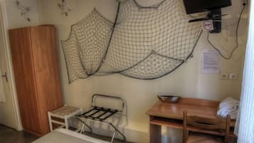 A compact room with a wooden wardrobe, a small table with a chair, a metal drying rack, and a television mounted on the wall.