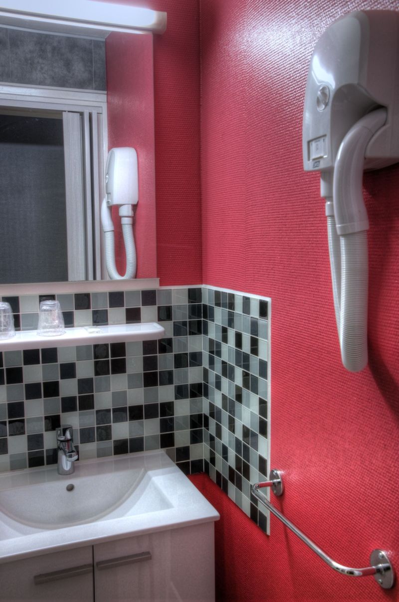 A bathroom with a white sink, a mirror, a hairdryer mounted on the wall, a tiled backsplash, and a red wall.