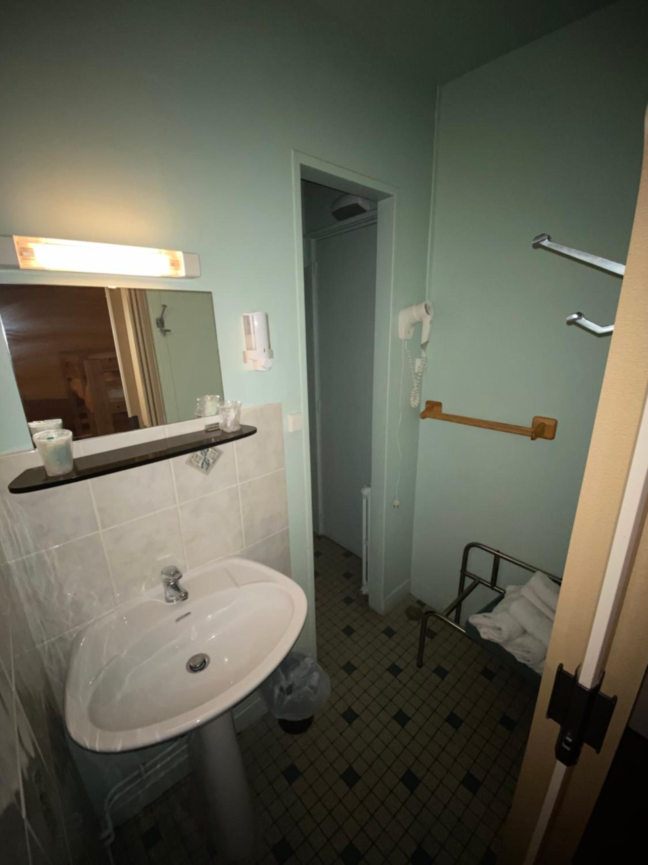 Een badkamer met een wastafel, spiegel, handdoekhouder en douchehoek.