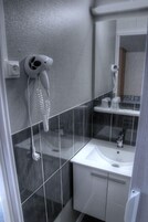 Un baño moderno con un lavabo blanco, un espejo y un secador de pelo fijado en la pared.