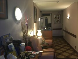 Un vestíbulo de hotel con una recepción, una zona de estar con una mesa y sillas, una planta decorativa y un cuadro en la pared.