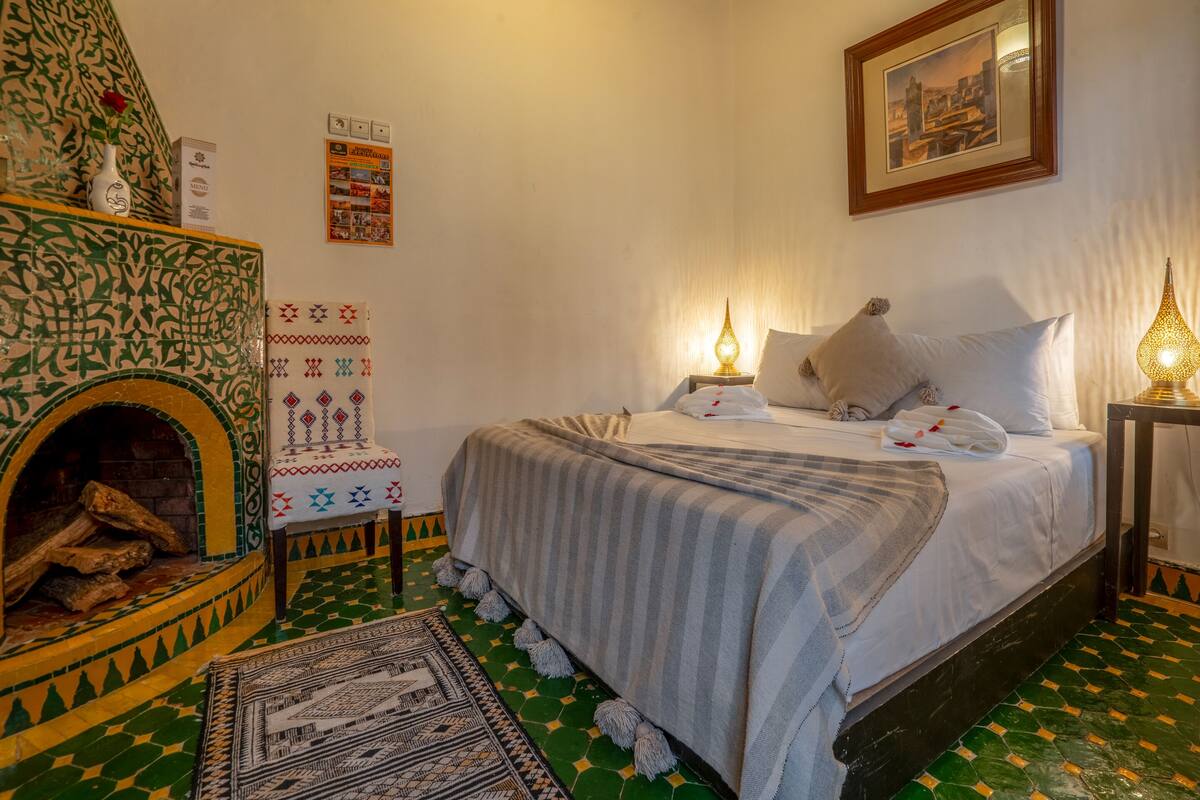 A room with a bed, a fireplace, a framed picture, and a wall with a menu board.