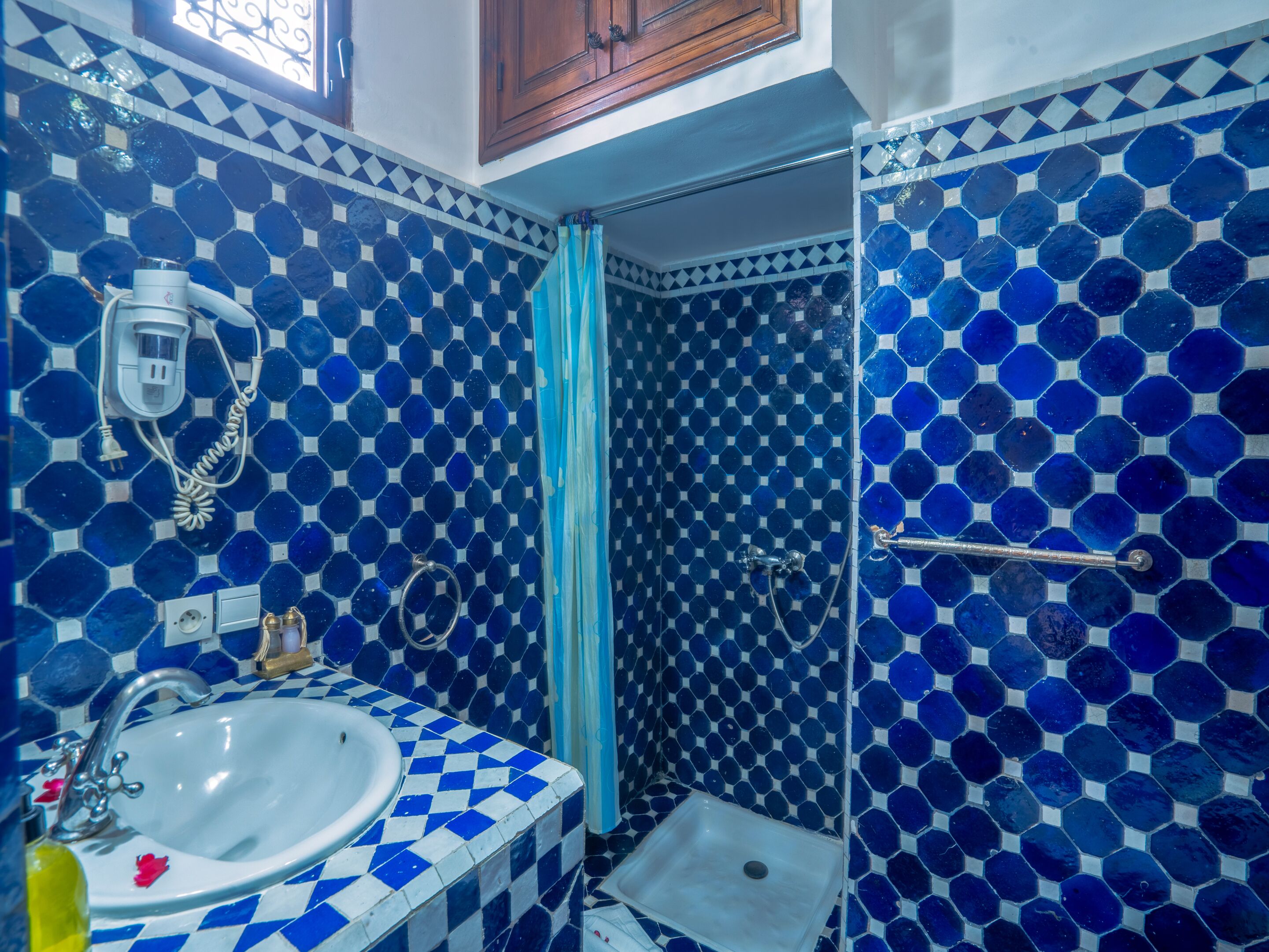 A bathroom with blue and white hexagonal tile walls, a white sink, and a shower area.