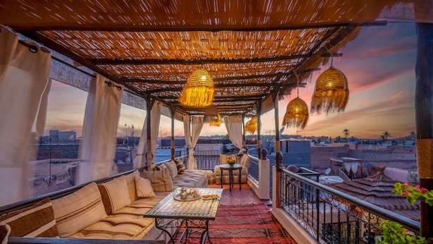 A cozy rooftop terrace with a thatched roof, cushioned seating, a small table with a teapot, and hanging lanterns. - Riad Sun of Kech (Marrakech)