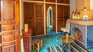 A traditional Moroccan interior with wooden doors, a tiled floor, a small seating area, and a decorative fireplace. - Riad Sun of Kech (Marrakech)