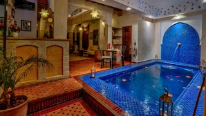 A luxurious indoor swimming pool with a blue mosaic wall, a wooden bench, and a potted plant. - Riad Sun of Kech (Marrakech)