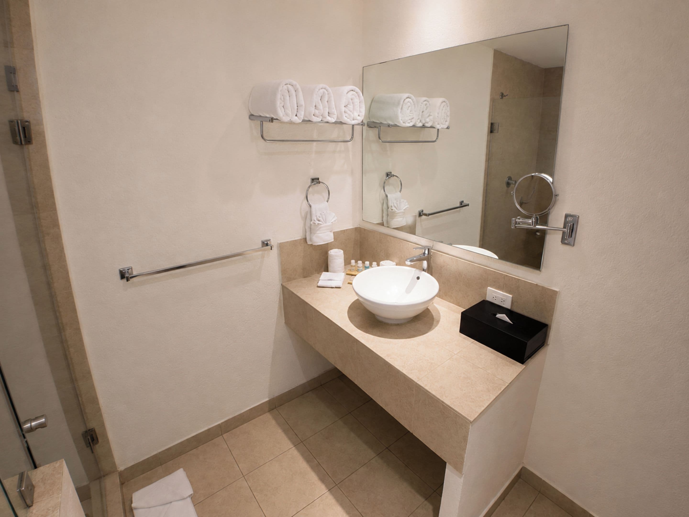Une salle de bain avec un comptoir beige, un lavabo blanc, un miroir et un porte-serviettes sur lequel sont pliées des serviettes.