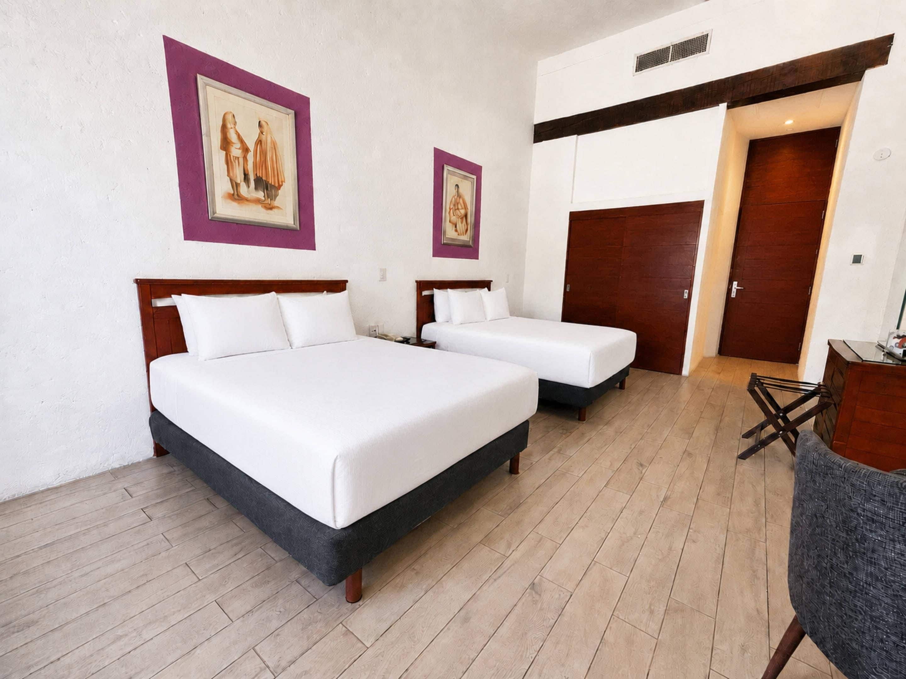 Habitación de hotel con dos camas, cabecero y suelo de madera, y una puerta.