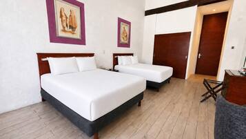 Habitación de hotel con dos camas, cabecero y suelo de madera, y una puerta.