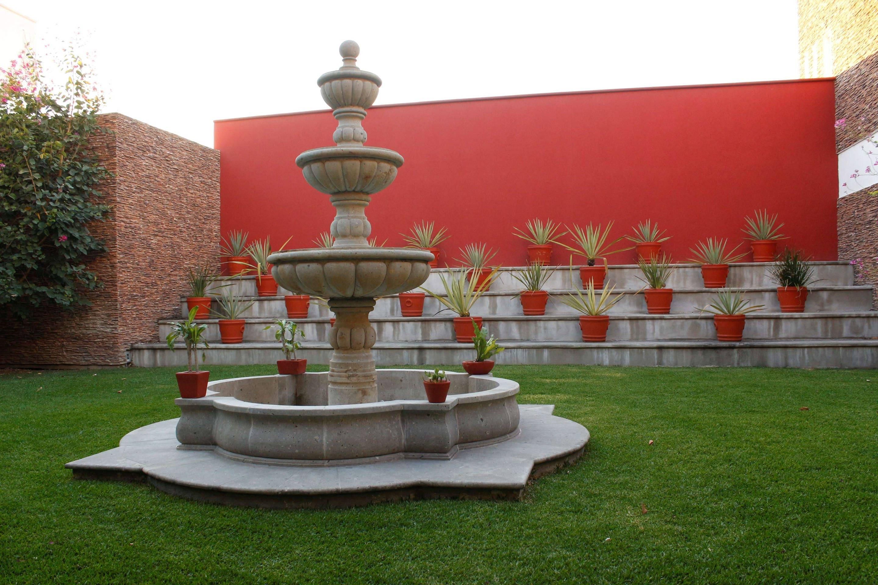 Una fuente de varios niveles en un patio con una pared roja y plantas en macetas.