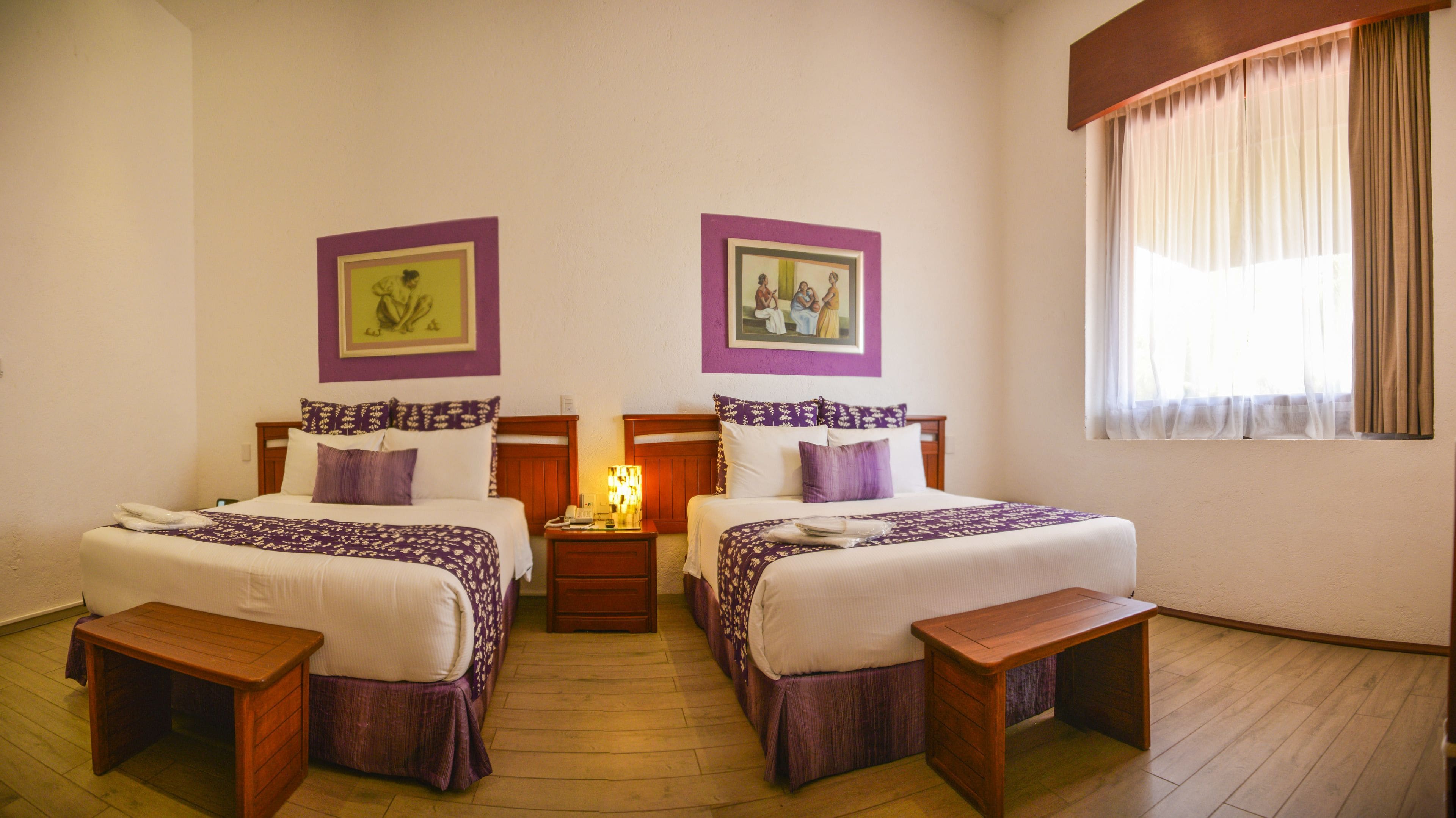 A hotel room with two beds, wooden nightstands, a bedside table, and a window with curtains.