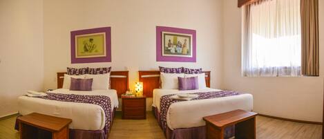 A hotel room with two beds, wooden nightstands, a bedside table, and a window with curtains.