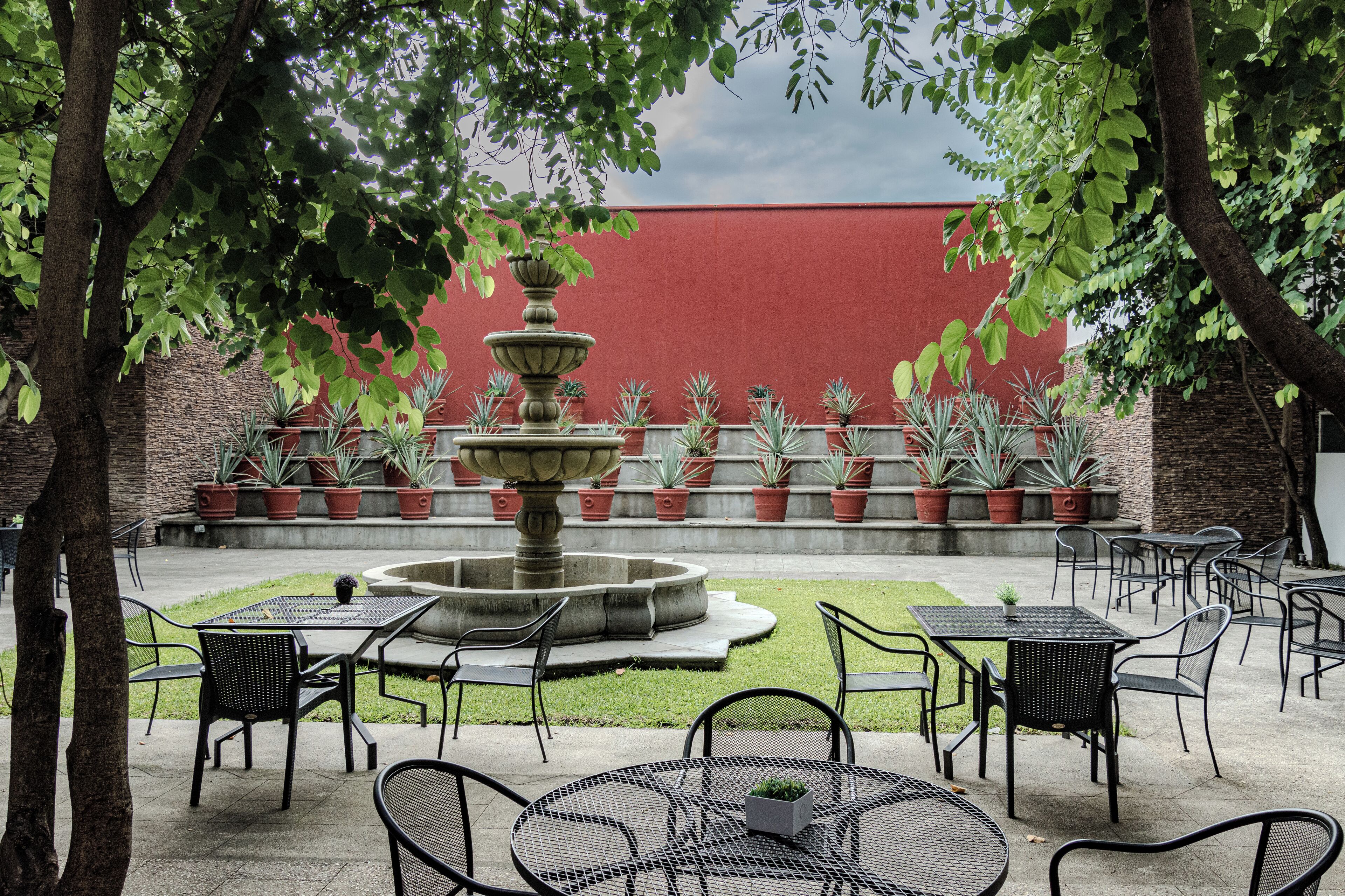 An outdoor patio area with a central fountain, surrounded by potted plants and outdoor seating.
