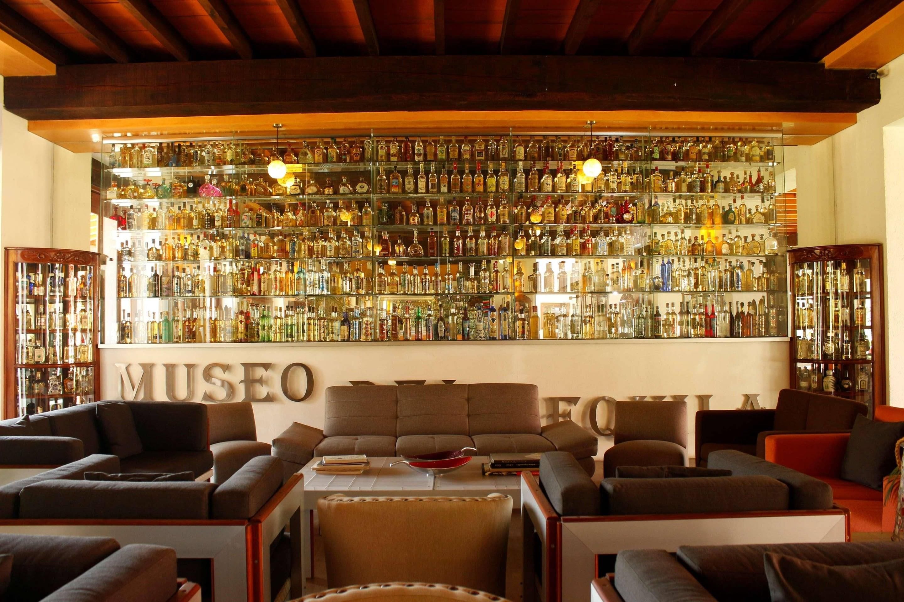 A bar area with a large wall of liquor bottles, sofas, and a sign reading 'MUSEO'.