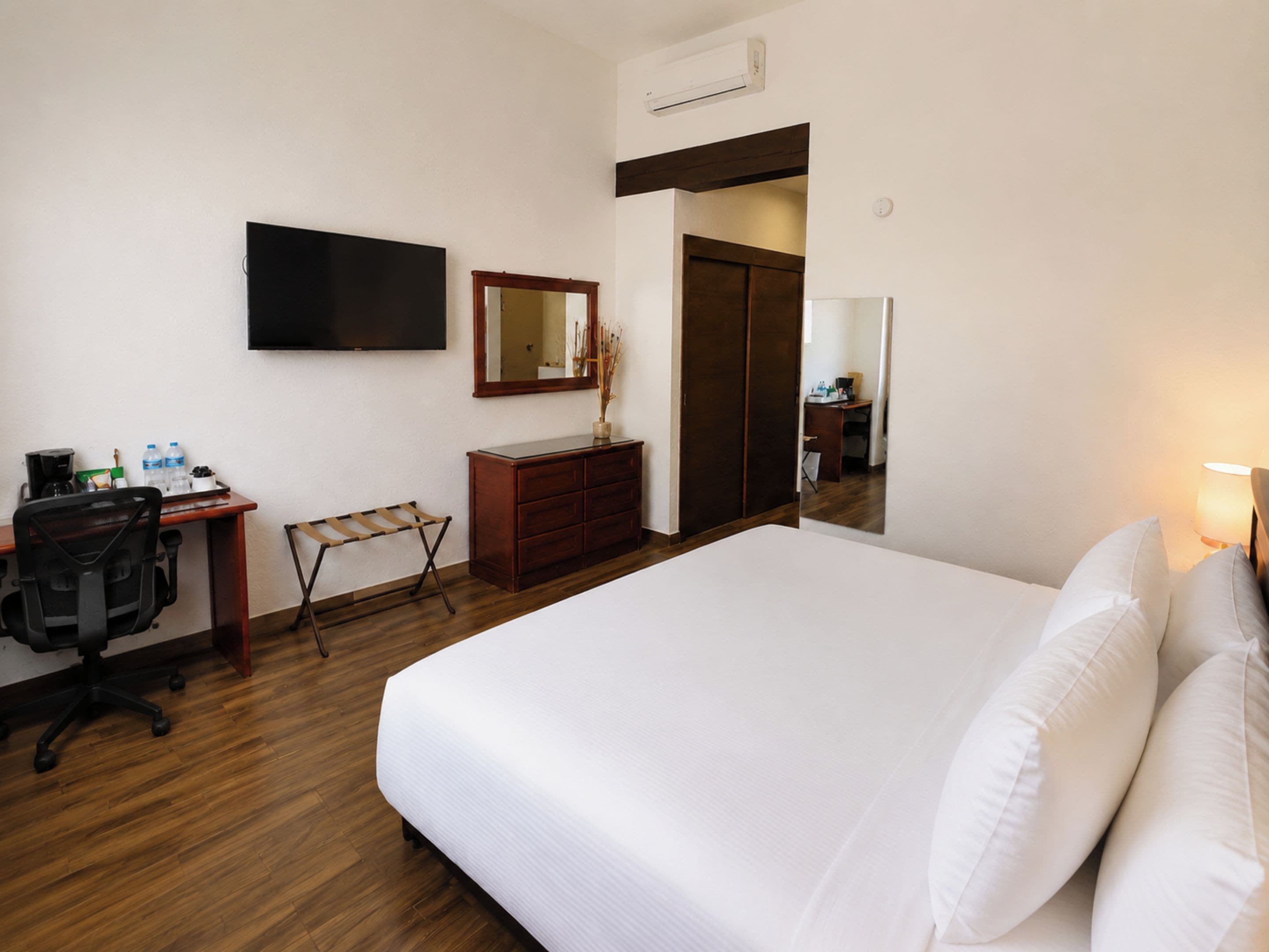 Una habitación de hotel con cama, escritorio, silla, cómoda, espejo y televisor.