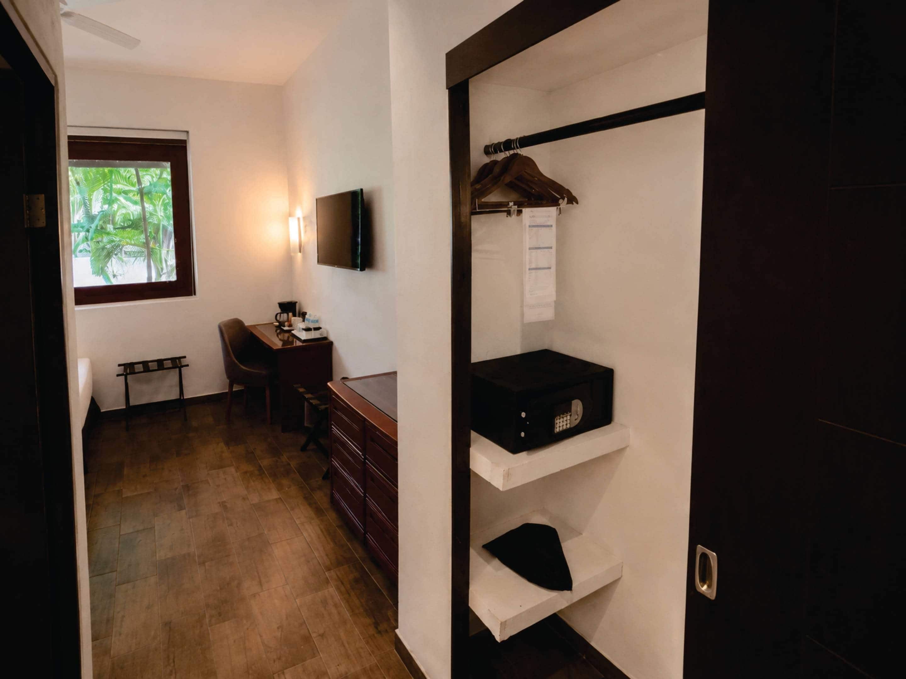 Habitación de hotel con escritorio, silla, televisor y armario con repisas.