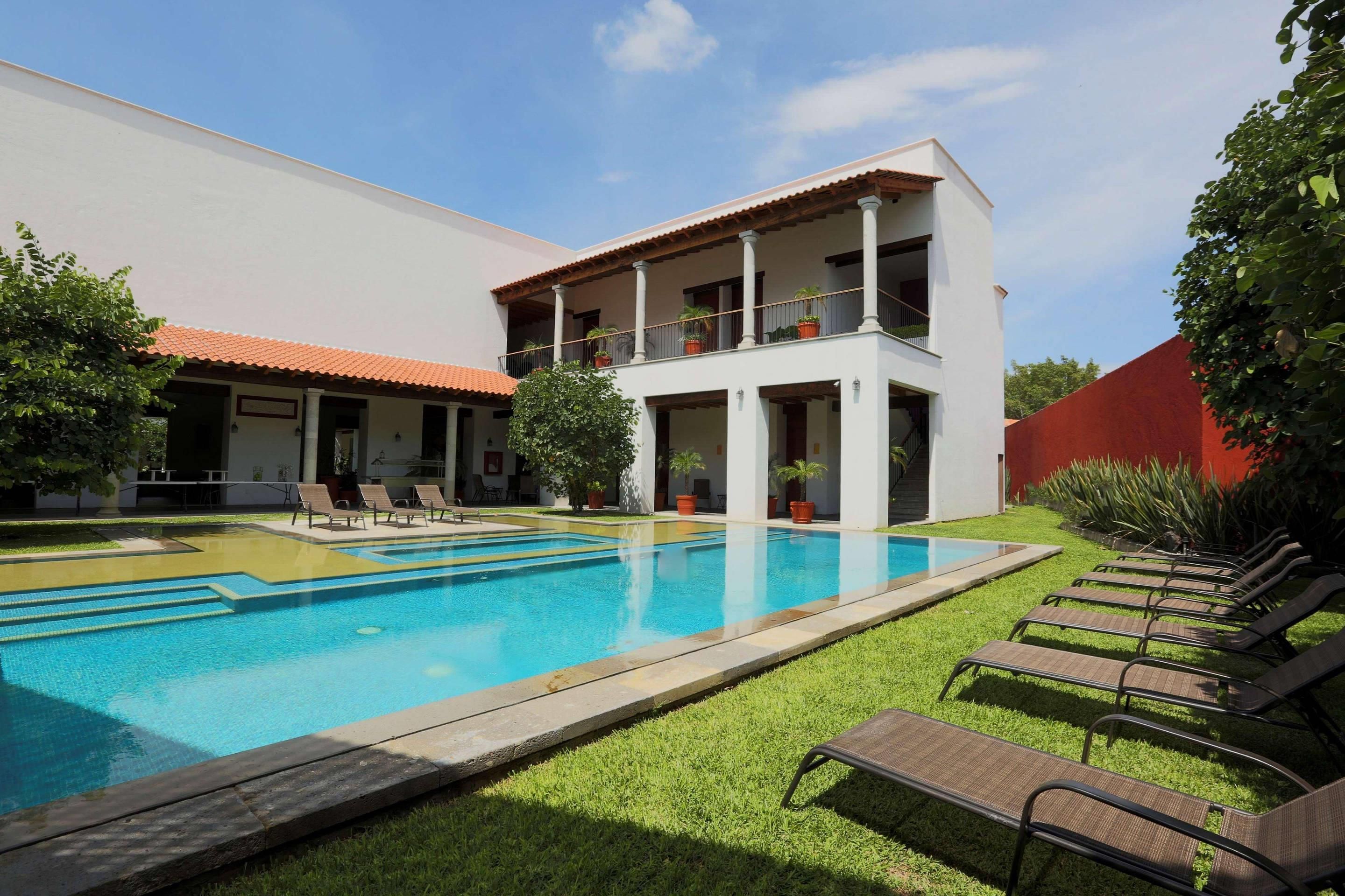 Un edificio de dos pisos con piscina y mobiliario exterior.