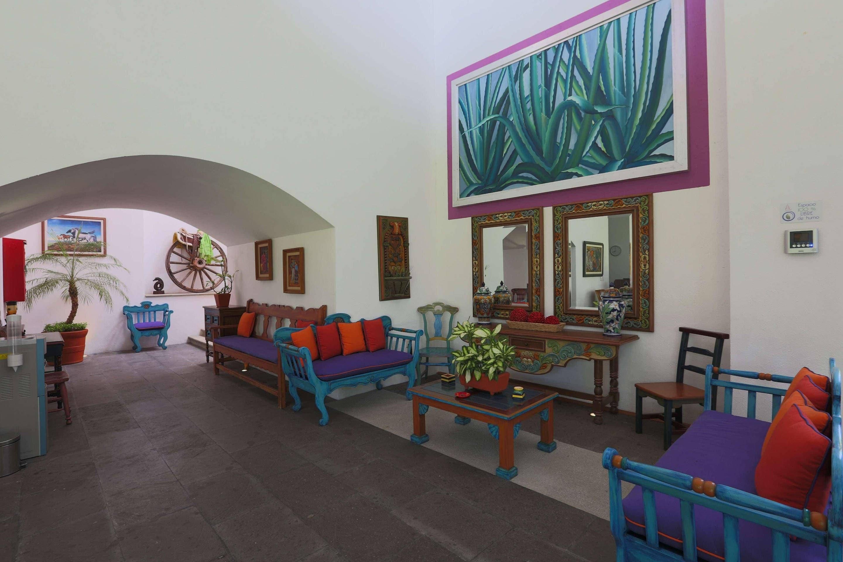 A spacious living area with a large painting, a wooden bench, a sofa with colorful cushions, and a table with a vase.
