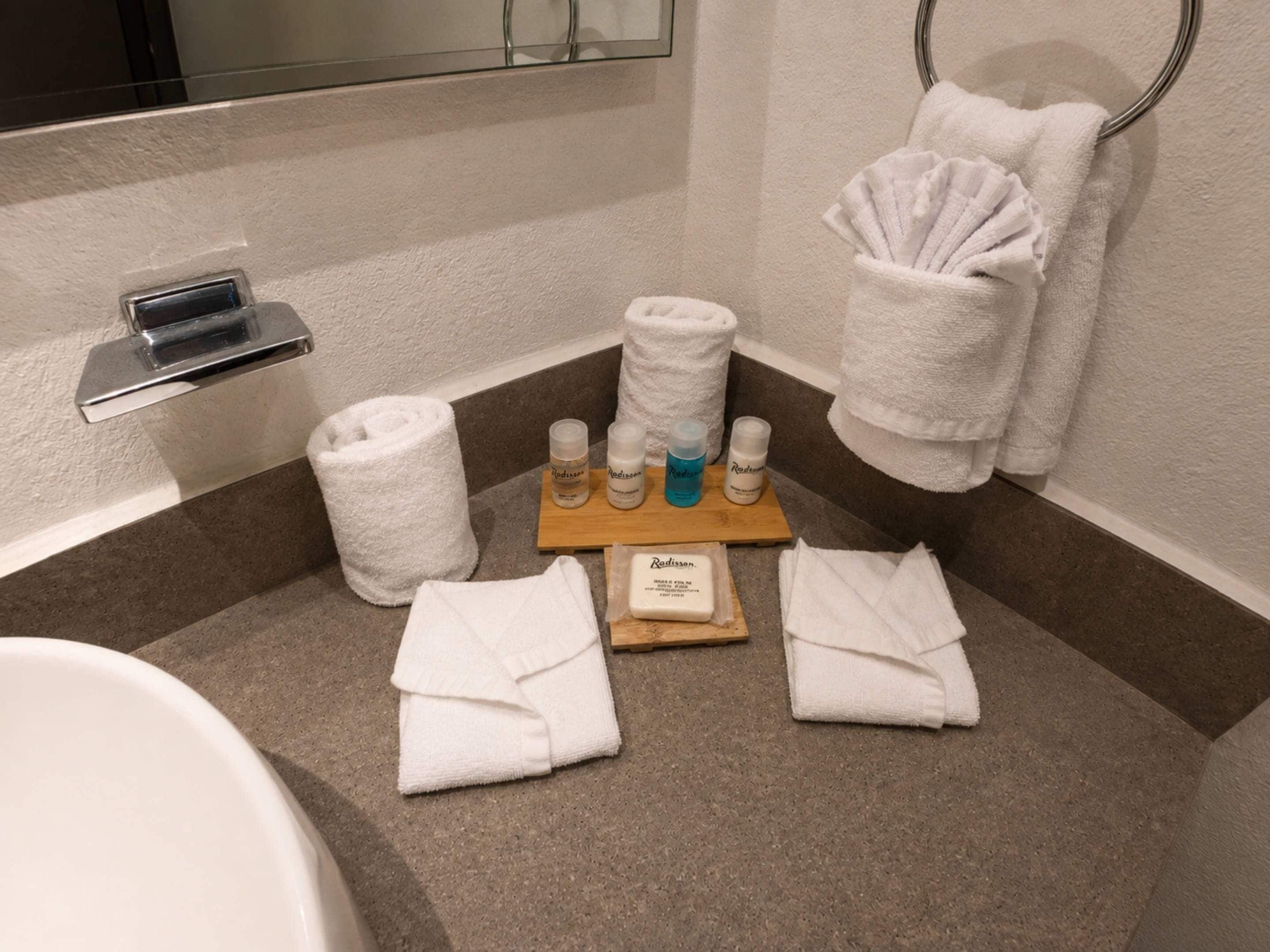 A bathroom with a bathtub, two towels, a hand towel, and a tray with toiletries.
