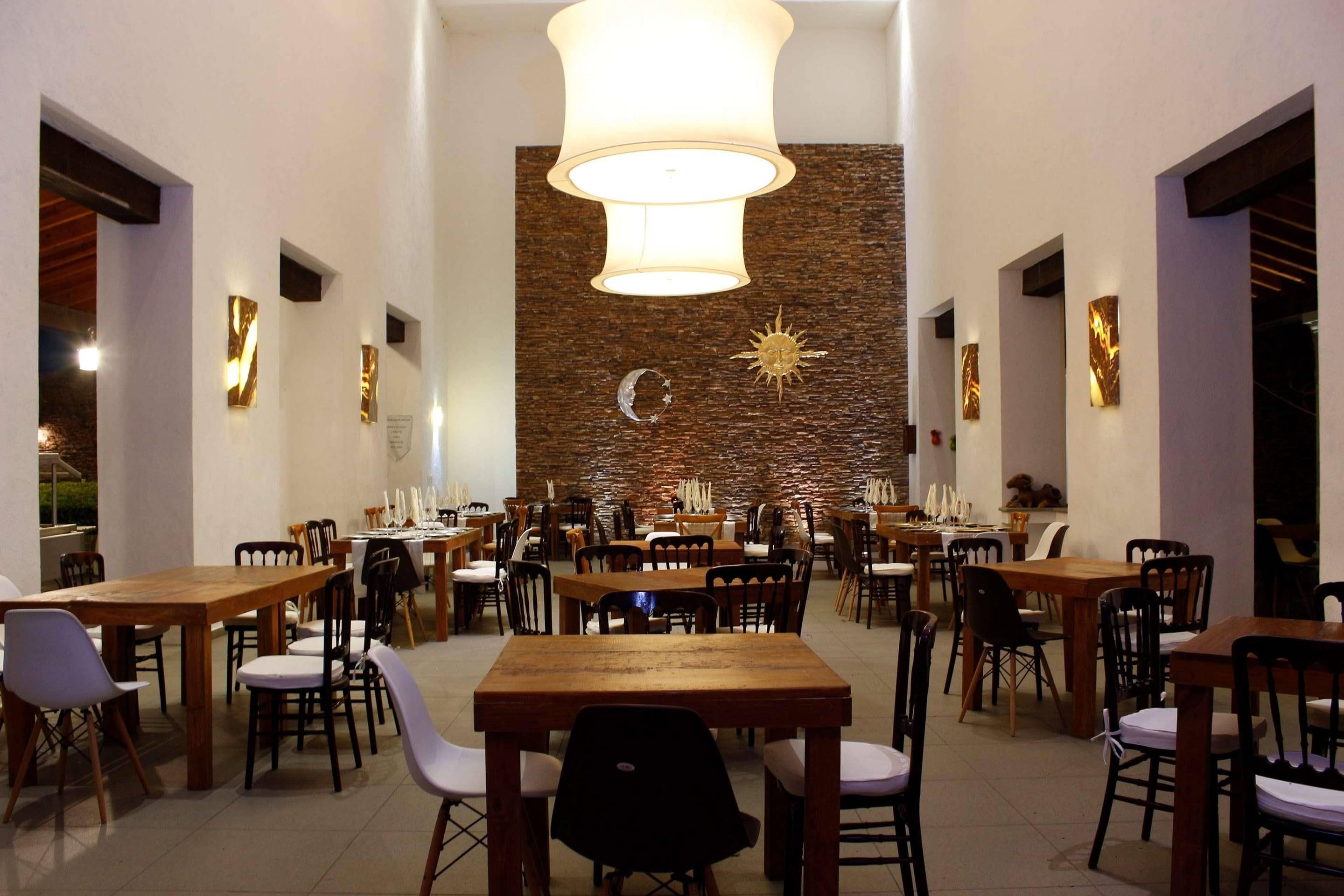 A dining area with multiple tables and chairs, a central chandelier, and a decorative wall with a sun and moon motif.