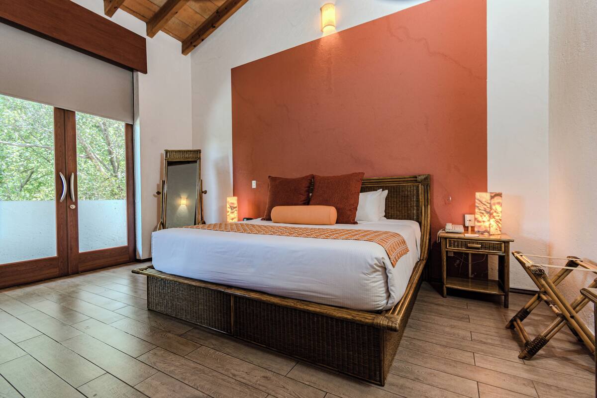 Une chambre à coucher avec un grand lit, un plancher en bois, une porte-fenêtre coulissante et une table de chevet avec une lampe.